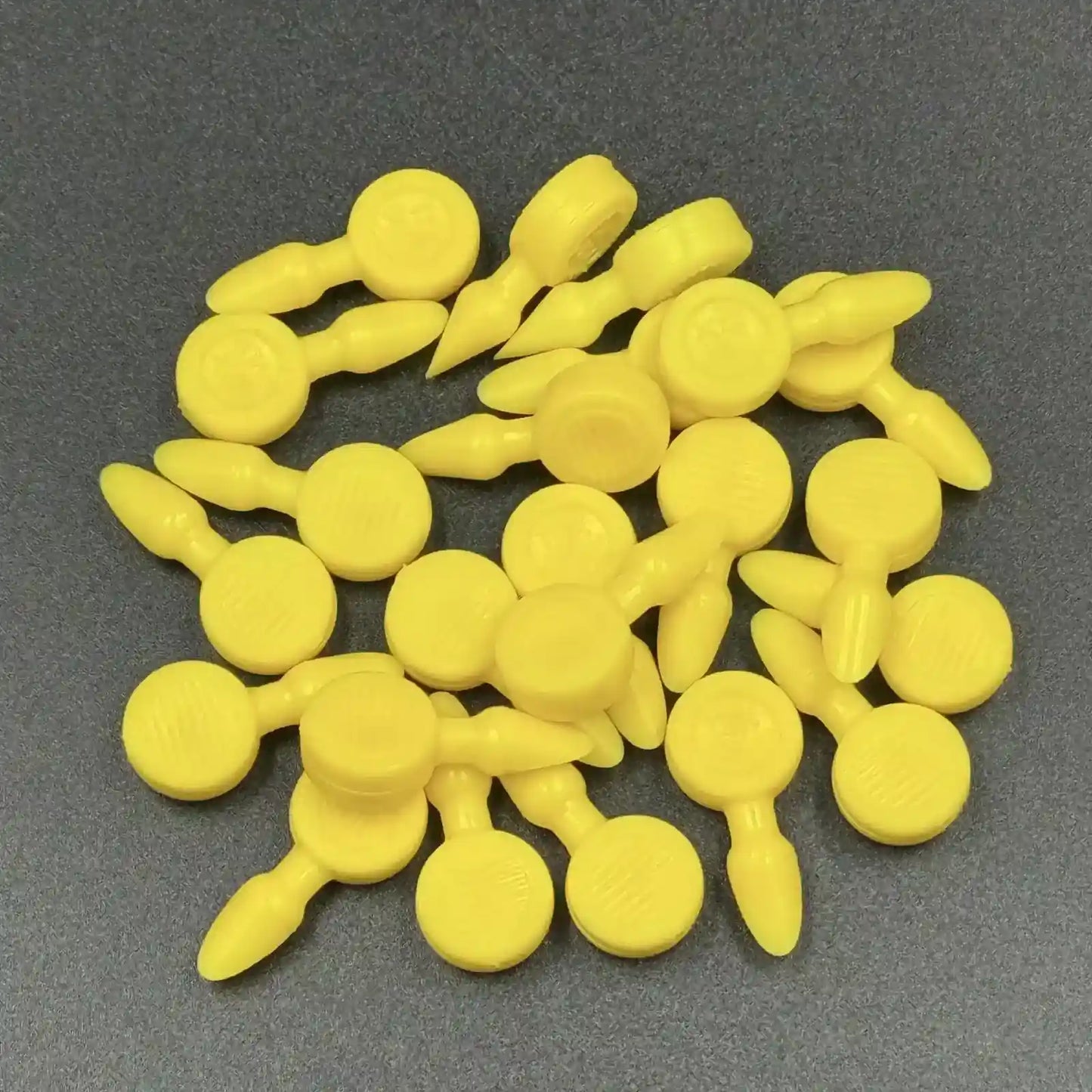 Texsolv Pfeilstecker in Gelb – Kunststoffstecker zur Fixierung von Texsolv Ösenschnur, rundes Design, auf dunkler Oberfläche lose angeordnet