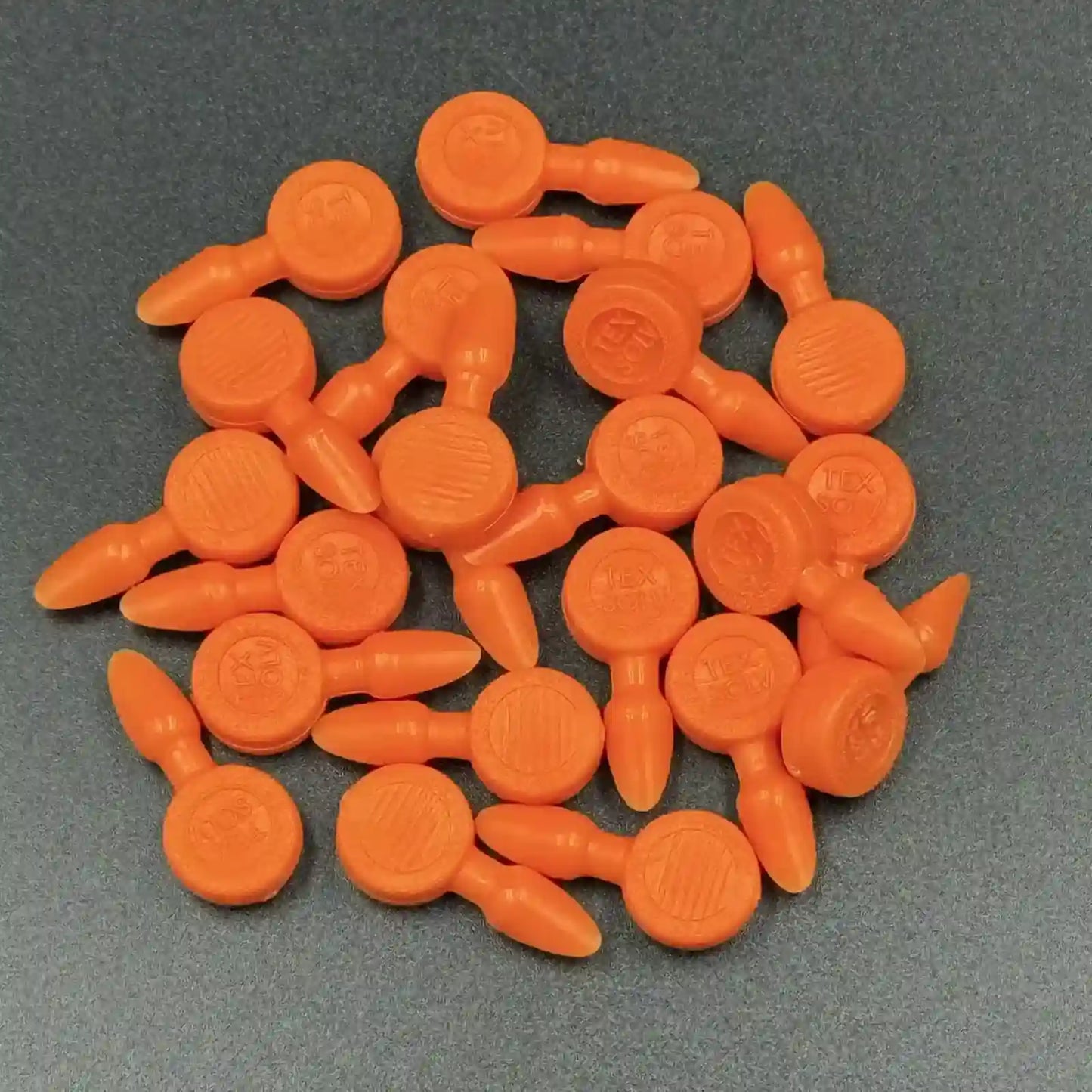 Texsolv Pfeilstecker in Orange – runde Kunststoffstecker zur Befestigung von Texsolv Ösenschnur am Webstuhl, flach auf dunklem Untergrund angeordnet
