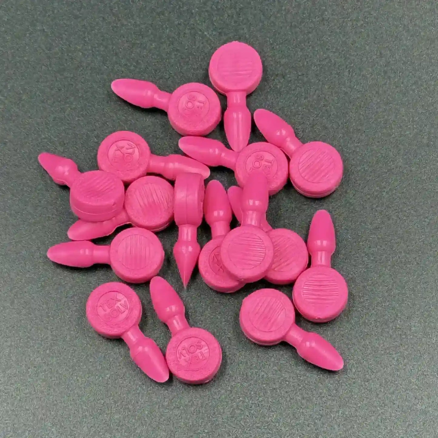 Texsolv Pfeilstecker in Pink – runde Kunststoffstecker zur Befestigung von Texsolv Ösenschnur am Webstuhl, flach auf dunklem Untergrund angeordnet