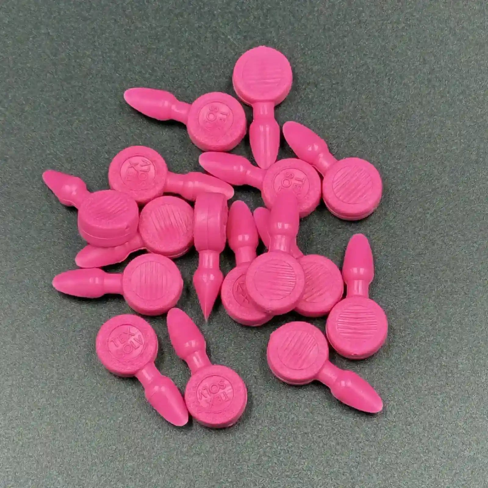 Texsolv Pfeilstecker in Pink – runde Kunststoffstecker zur Befestigung von Texsolv Ösenschnur am Webstuhl, flach auf dunklem Untergrund angeordnet