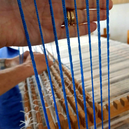 Hand hält blaue Texsolv Schlaufenschnüre vor eingesetzten Litzen – visuelle Qualitätskontrolle am Webstuhl