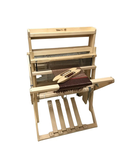 Toika Anni Bodenwebstuhl – Frontansicht mit eingelegtem Schiffchen und gewebtem Stoff, kompakter Vier-Schaft-Webstuhl aus hellem Holz